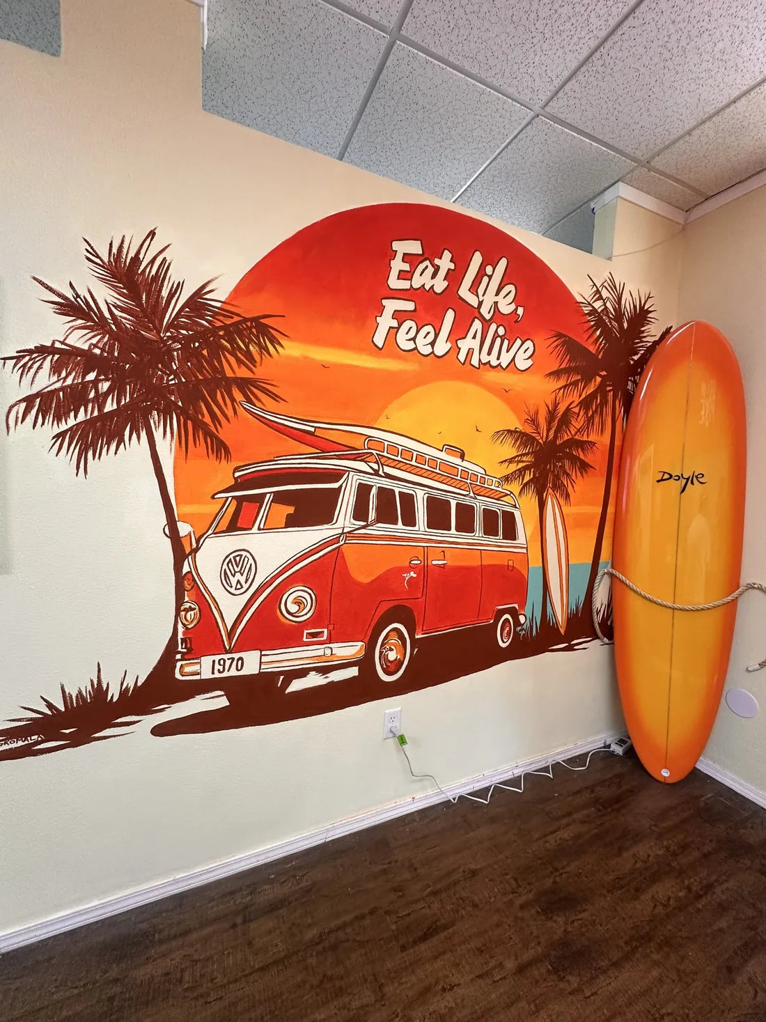 A mural of a red van under palm trees and a big sun