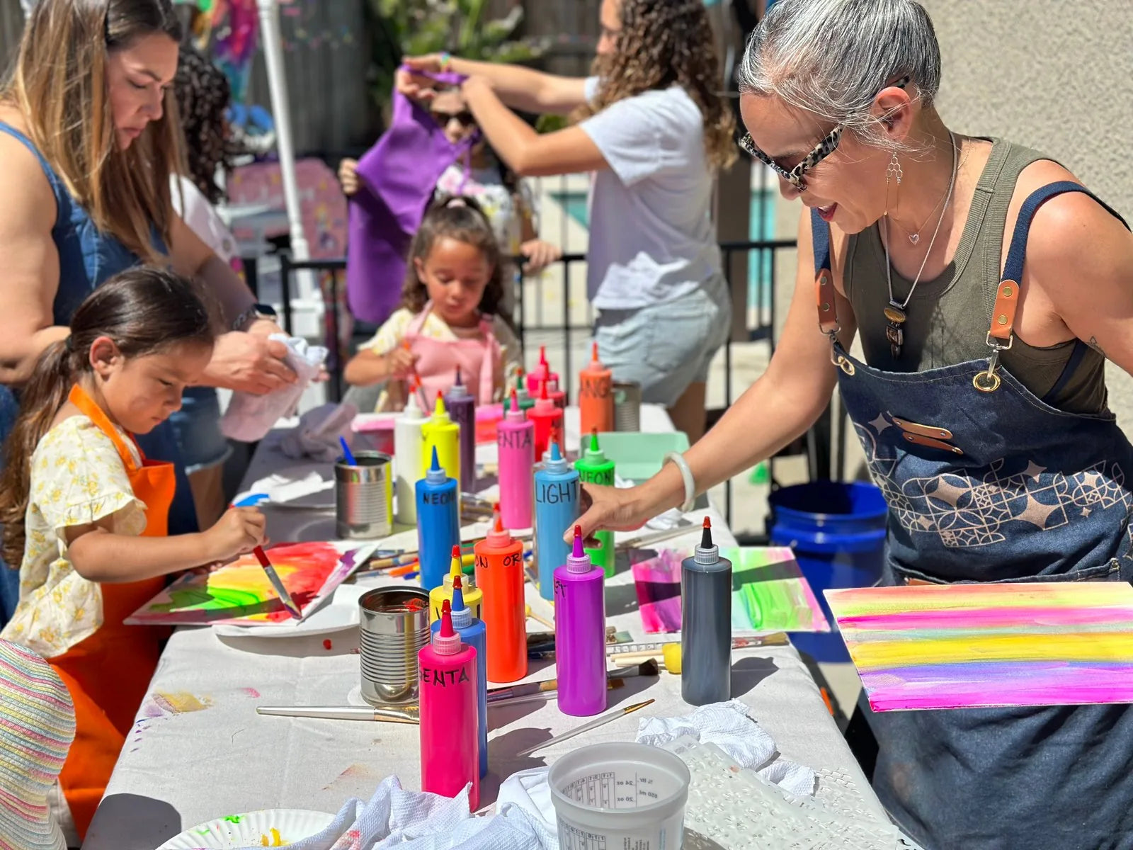 Kids painting at a long table with bright paint bottles