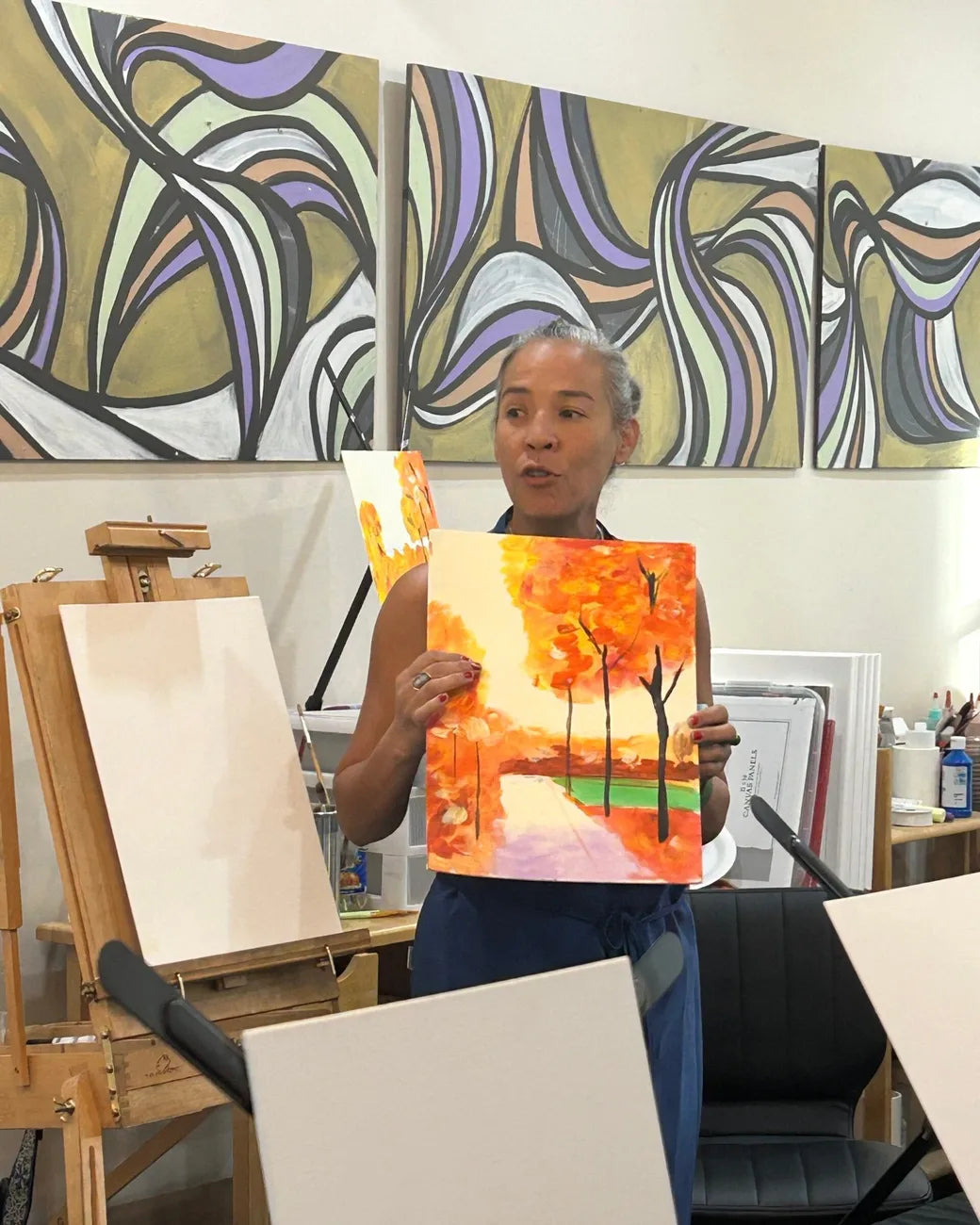 Showing an orange fall painting in the studio, with large wall paintings behind