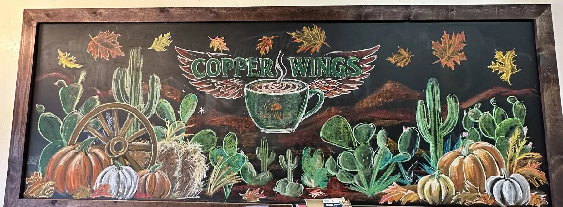 A fall chalk board with cactus, pumpkins and a wagon wheel